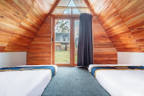 A room with wooden sloped ceilings, two beds with matching bedding, a large sliding glass door, and a view of the outdoors.