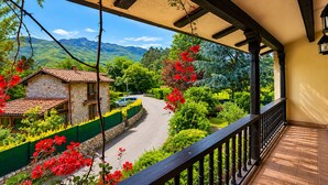 Un balcone con vista su una strada, del verde e un edificio in pietra.