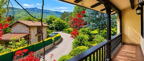 En balkon med udsigt over en vej, grøn vegetation og en bygning i sten.