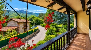 Ein Balkon mit Blick auf eine Straße, Grünflächen und ein Steinhaus.