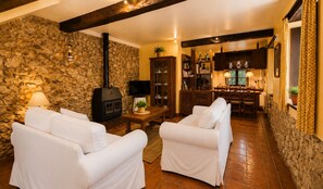 Ein gemütliches Wohnzimmer mit Steinwänden, einem Kamin, weißen Sofas und einem Essbereich.