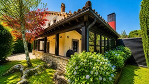 Un edificio tradizionale con un portico coperto, pareti in pietra e un giardino con macchie di ortensie.