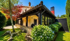 Ein traditionelles Gebäude mit überdachter Terrasse, Steinmauern und einem Garten mit Hortensienbüschen.