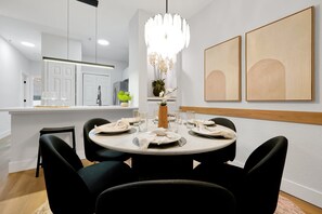 A modern dining area with a round table set for four, surrounded by black chairs. - Legacy Dunes Retreat Near Disney (Kissimmee)