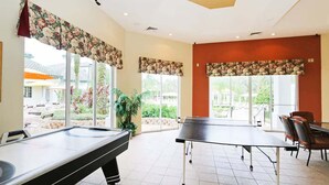 A pool table and billiards equipment in a room with large windows, a potted plant, and a dining area with chairs. - Legacy Dunes Retreat Near Disney (Kissimmee)