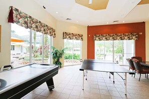 A pool table and billiards equipment in a room with large windows, a potted plant, and a dining area with chairs. - Legacy Dunes Retreat Near Disney (Kissimmee)