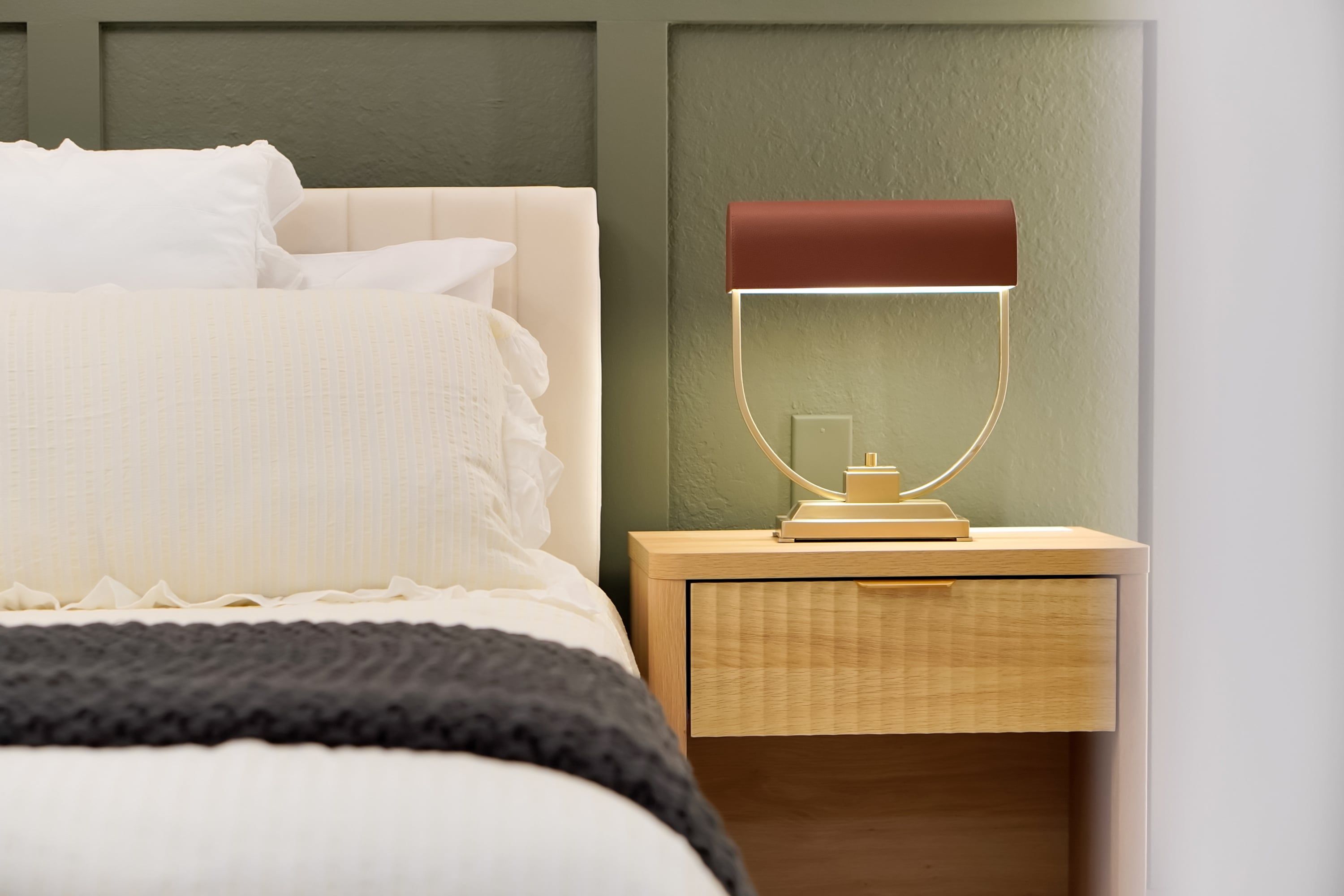 A neatly made bed with white bedding, a bedside table with a lamp, and a wooden nightstand.
