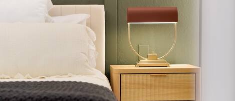 A neatly made bed with white bedding, a bedside table with a lamp, and a wooden nightstand.