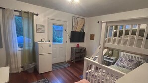 Habitación compacta con una cuna, un escritorio pequeño, una silla, un tapete y una ventana con cortinas.