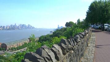 A stone wall with a paved walkway, overlooking a body of water and a distant city skyline.