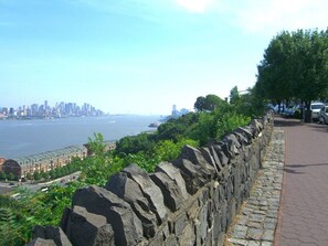Eine Steinmauer mit einem gepflasterten Weg, mit Blick auf ein Gewässer und eine entfernte Stadtlandschaft.