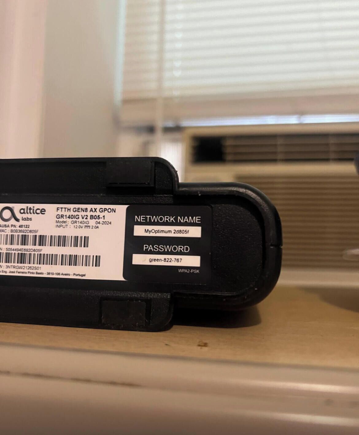 A black printer with a label indicating it is a FTTH GEN8 AX GPON model, network name, and password.