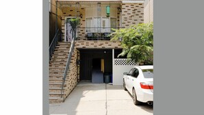 Edificio de dos pisos con fachada de ladrillo, un porche cubierto, una escalera y un coche blanco estacionado en la entrada.
