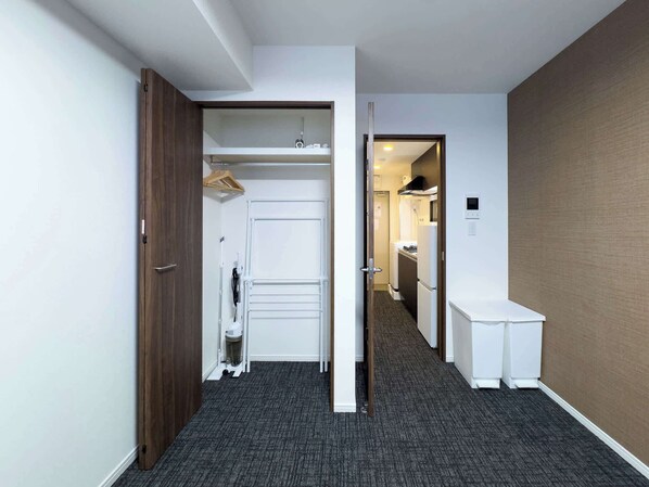 A hallway with a wardrobe, a small trash bin, and a kitchenette area.