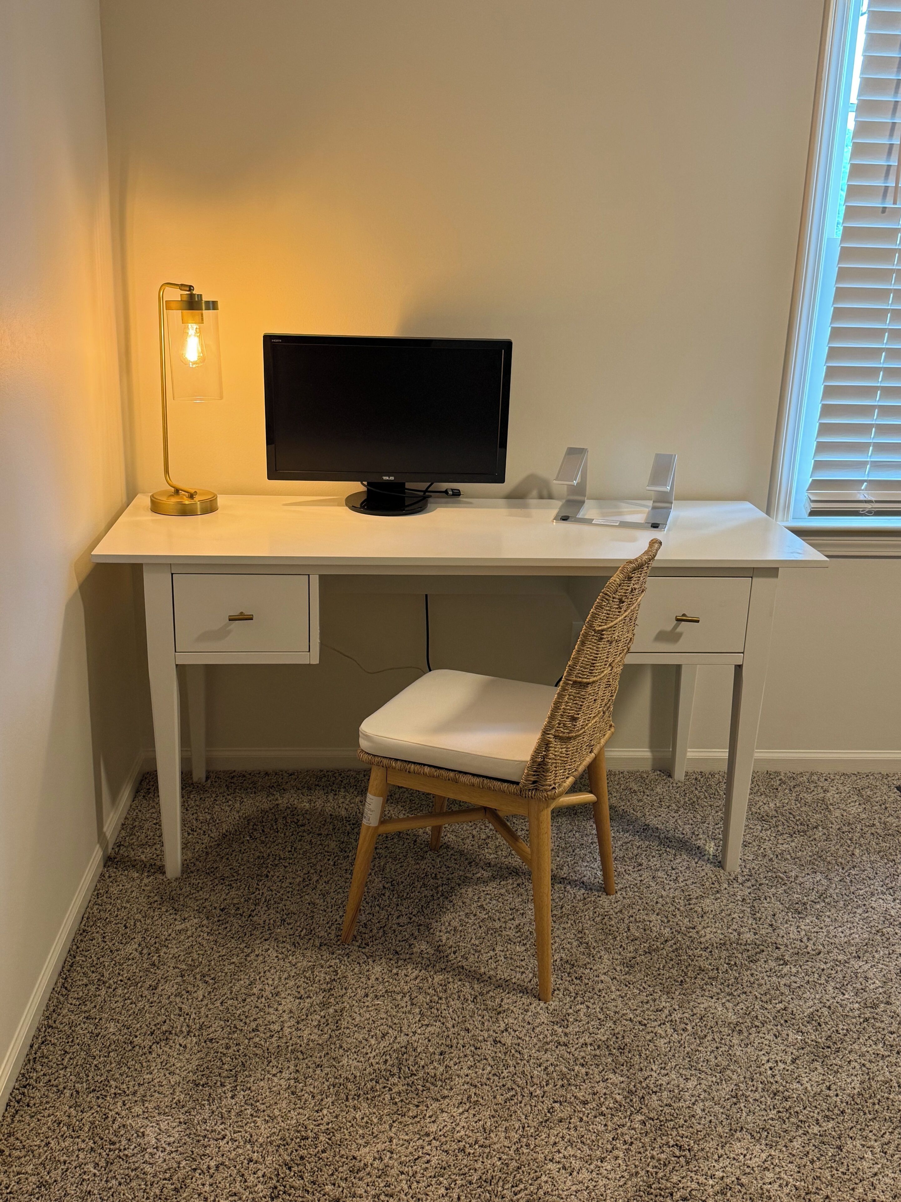 A white desk with a computer monitor, a lamp, and a chair.
