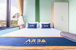 Habitación de hotel con cama, dos almohadas con el logotipo de 'ARBA Hospitality', un ventanal con cortinas y un armario.