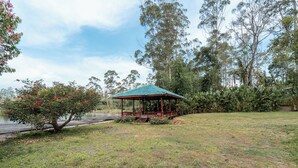 Ein Gazebo mit grüner Dachfläche in einer grünen Parklandschaft mit Bäumen und einem Gewässer.