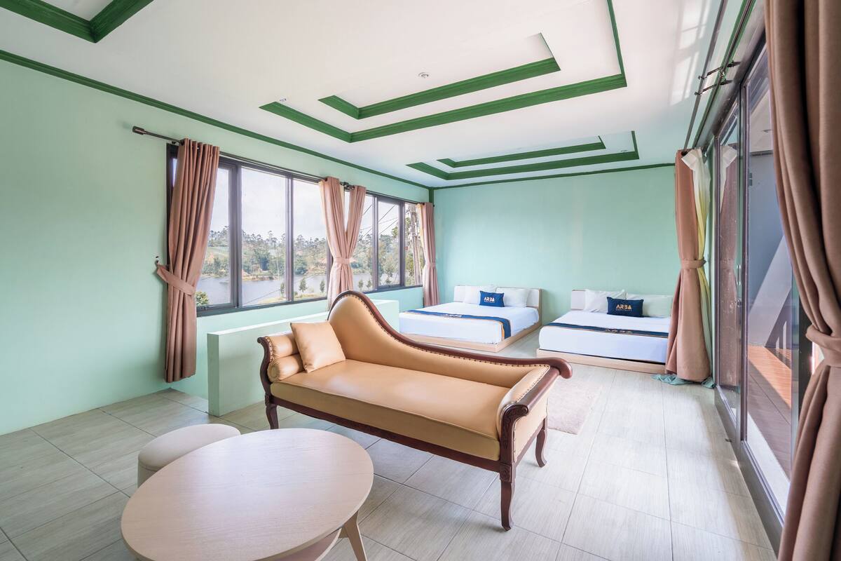 A room with a sofa, a table, a bed, and large windows.