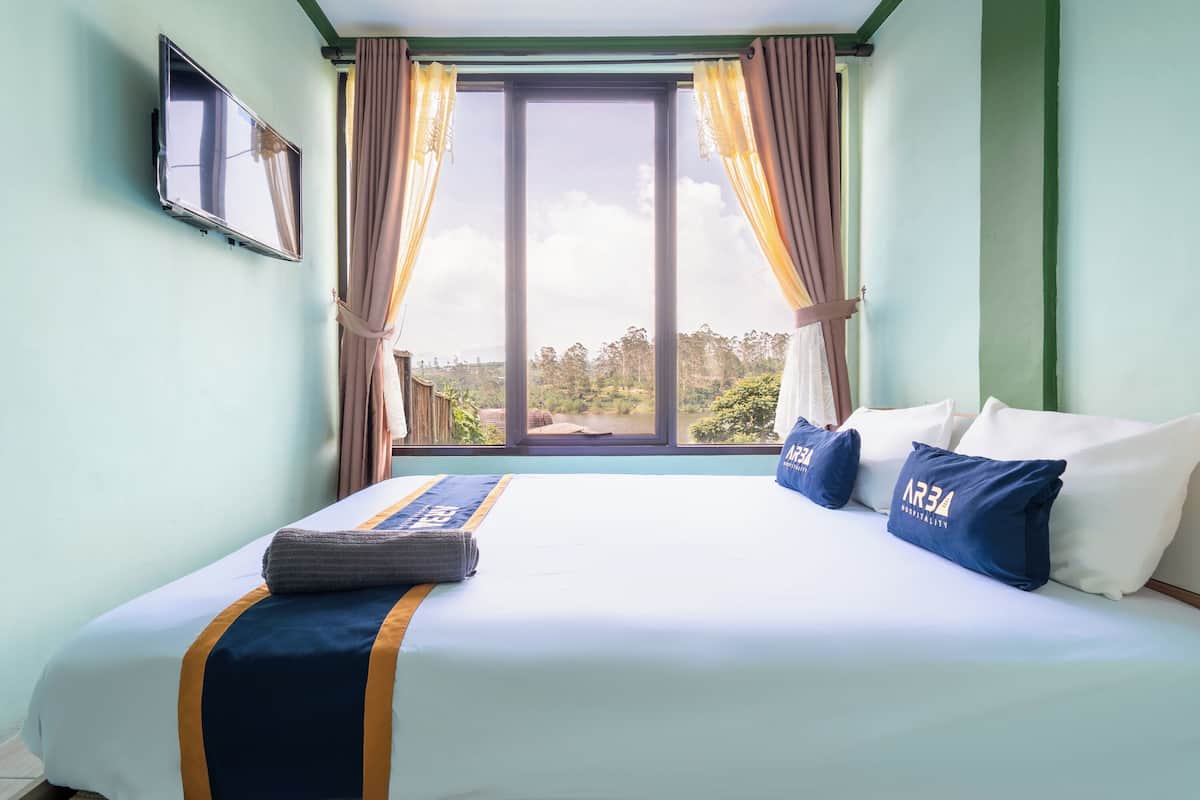 A hotel room with a bed, curtains, a window, and a flat-screen TV.