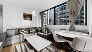 Een moderne woonkamer met een grijze bank, een witte salontafel en een eettafel met stoelen.