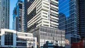 Een modern hoog gebouw met een opvallende glazen gevel, omringd door andere hoge gebouwen.