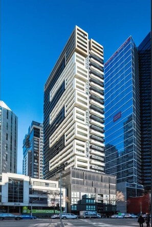 Ein modernes Hochhaus mit einer auffälligen Glasfassade, umgeben von weiteren hohen Gebäuden.