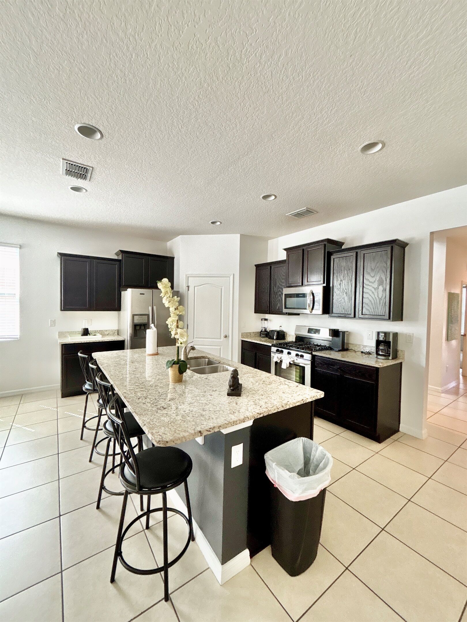 Une cuisine moderne avec un îlot central, des meubles de couleur sombre et un sol carrelé.