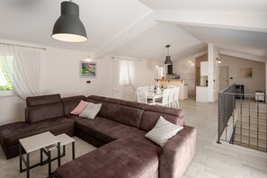 Ein modernes Wohnzimmer mit einer Eckcouch, einem Essbereich und einer Küche im Hintergrund.