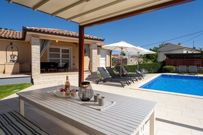 Ein Poolbereich mit Liegestühlen, einem Tisch mit Getränken und einer überdachten Terrasse.