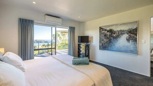 Quarto de hotel com uma cama grande, televisão, pintura e vista para um corpo de água.