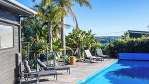 Piscina com espreguiçadeiras, deck de madeira e plantas tropicais.