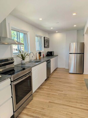 Une cuisine moderne dotée d’appareils électroménagers en acier inoxydable, de meubles blancs et d’un plancher en bois.