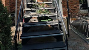 Een woongebouw met een trap die leidt naar een balkon, een bakstenen gevel en een kleine tuin.
