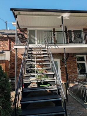 Un immeuble résidentiel doté d’un escalier menant à un balcon, avec une façade en briques et un petit espace jardin.