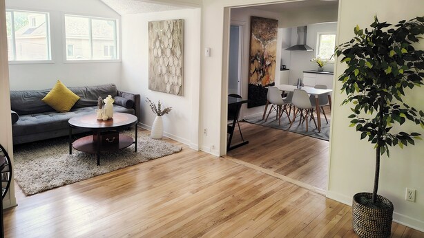 Een moderne woonkamer met een grijze bank, een salontafel en een eethoek met een witte tafel en stoelen.