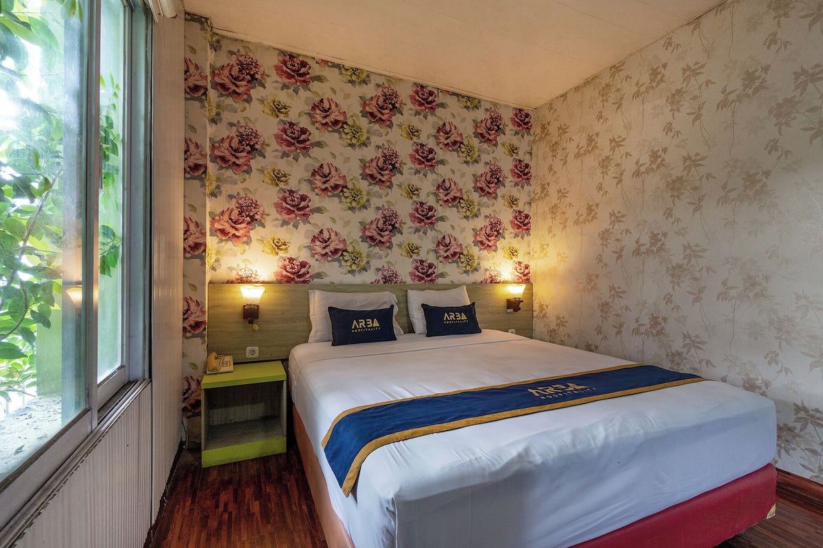Une chambre d’hôtel avec un lit, un papier peint à motifs floraux, des lampes de chevet et une fenêtre.