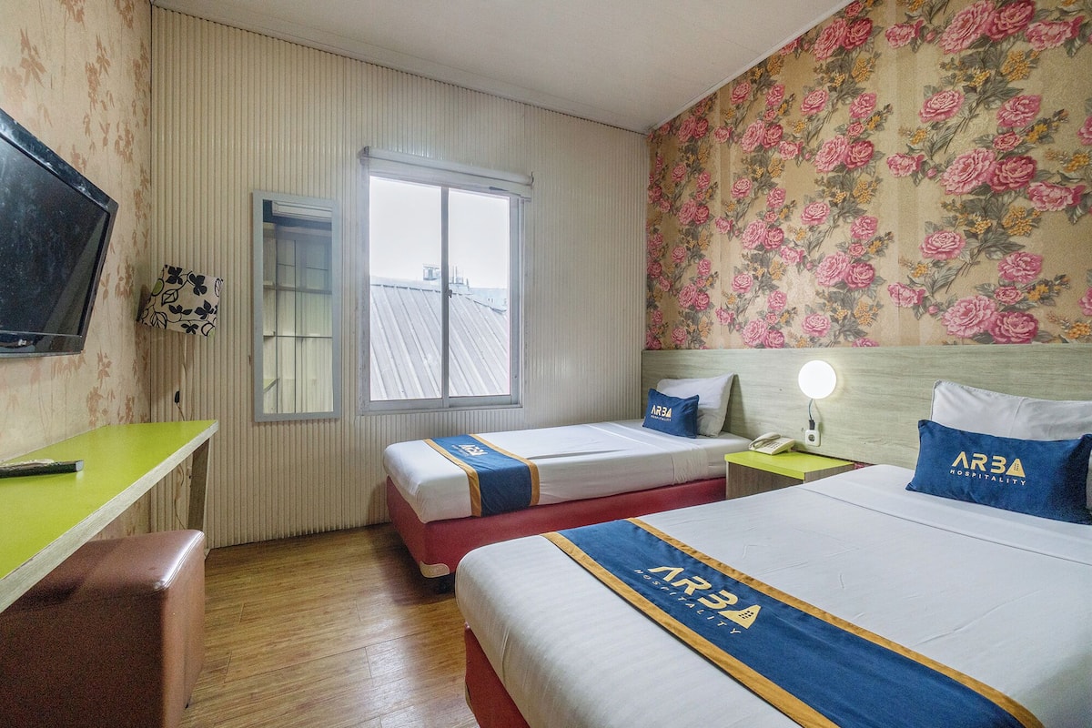 Une chambre d’hôtel avec deux lits, une télévision, une fenêtre et un papier peint à motifs floraux.