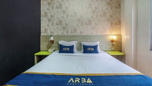 Een hotelkamer met een bed, twee kussens met 'ARBA HOSPITALITY' branding, een bedtelefoon en een wandlamp.