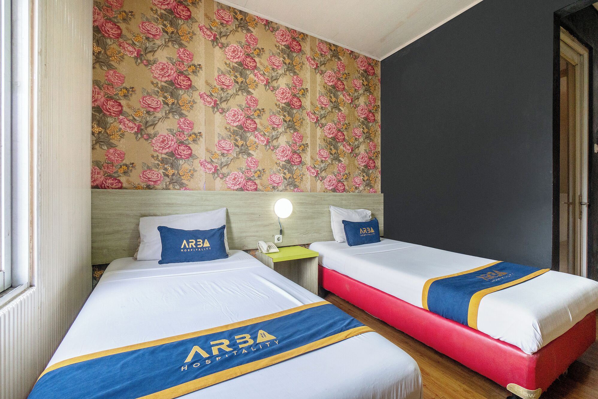 Two beds with matching headboards, a nightstand with a lamp, and a floral wallpaper.