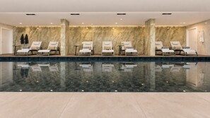 Zona d'spa amb una piscina gran, nombroses gandules i una paret de marbre.