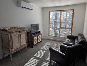 A room with a television on a wooden cabinet, a large window with blinds, and a leather sofa. - Charming Home in Ballarat near Sovereign Hill (Mount Pleasant)