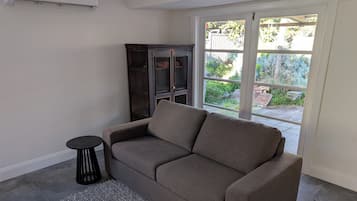 Een woonkamer met een grijze bank, een klein rond tafeltje en een donker houten kast.