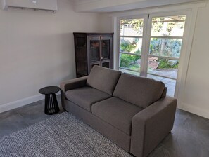 A living room with a grey sofa, a small round table, and a dark wooden cabinet.