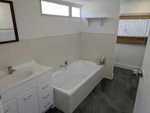 Un baño con bañera, dos lavamanos, un espejo y una ventana.