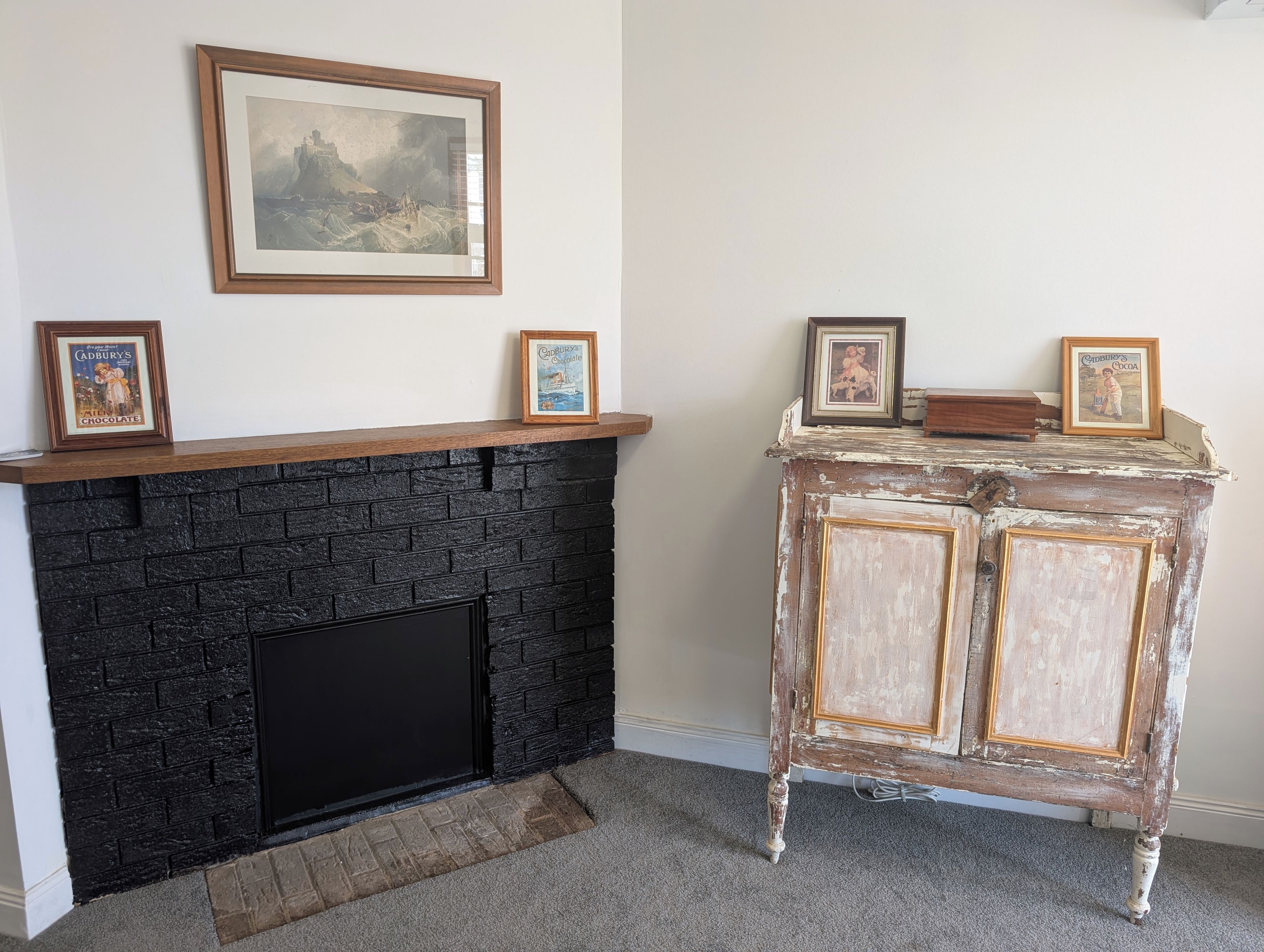 A fireplace with a black brick facade, a mantel with framed pictures, and a white wall.
