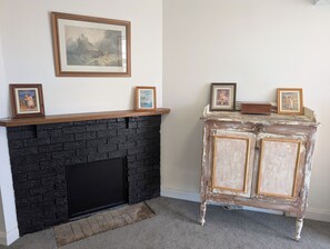 A fireplace with a black brick facade, a mantel with framed pictures, and a white wall.