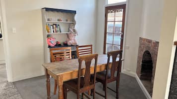 Een eetgedeelte met een houten tafel en stoelen, een boekenkast met boeken en een knuffel, en een open haard van baksteen.