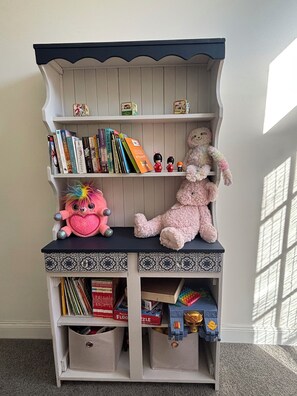 A bookshelf with books, toys, and a stuffed animal.