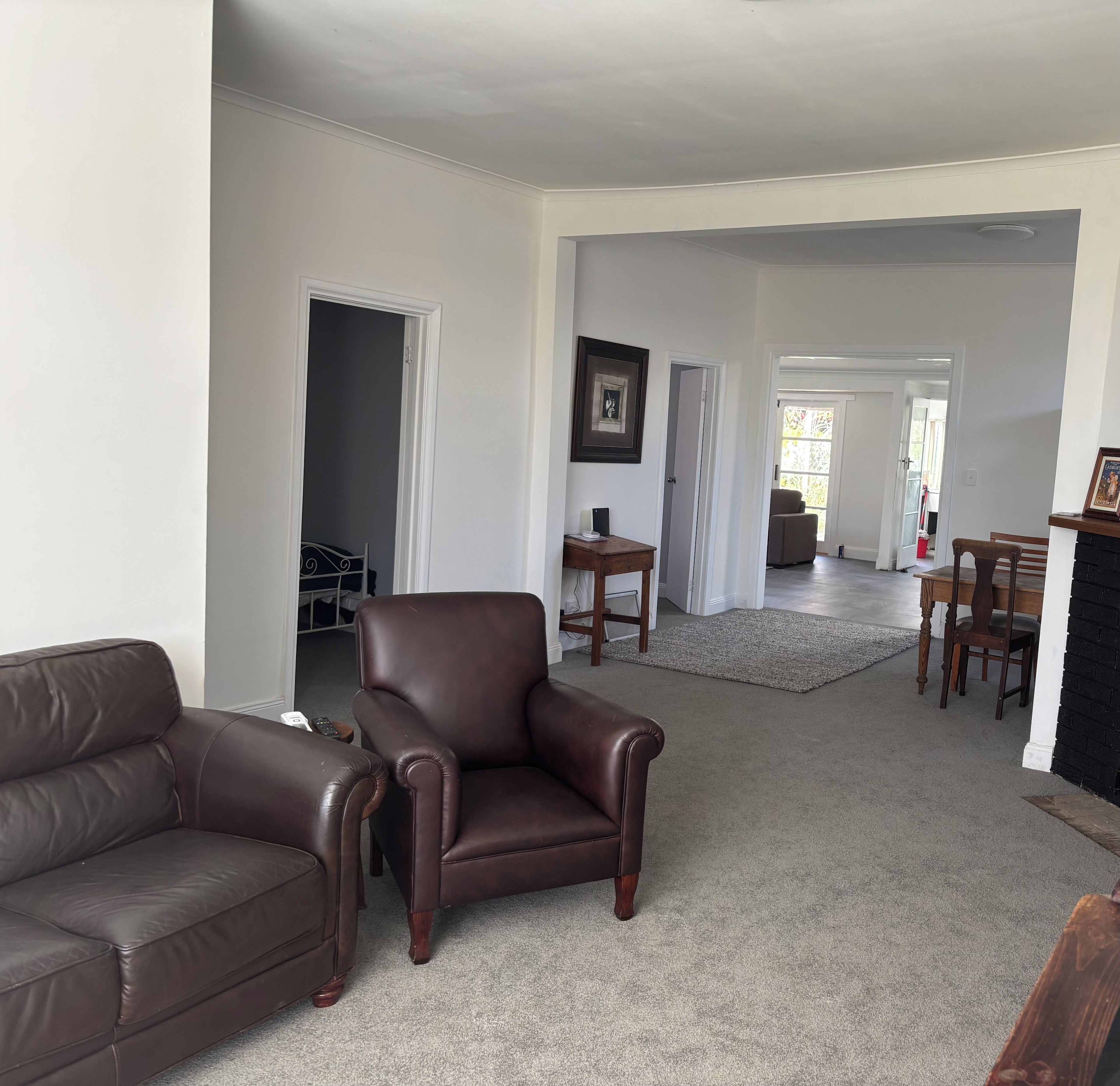 A spacious living room with a leather sofa, a leather armchair, and a dining area with a table and chairs.