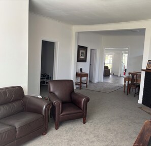 A spacious living room with a leather sofa, a leather armchair, and a dining area with a table and chairs.